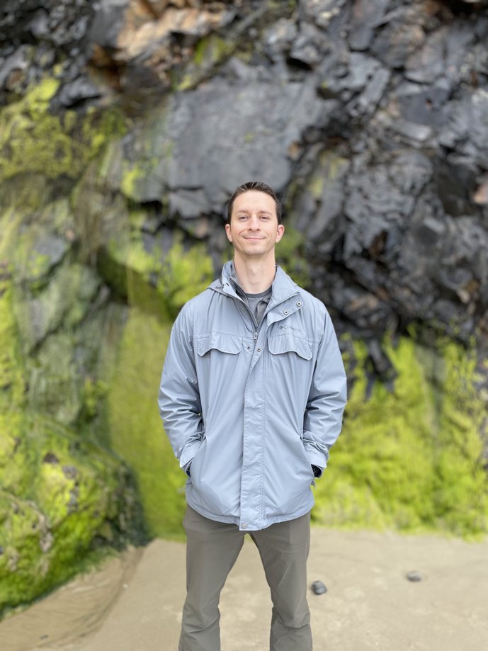 Man standing in front of moss covered rocks on the Oregon coast.